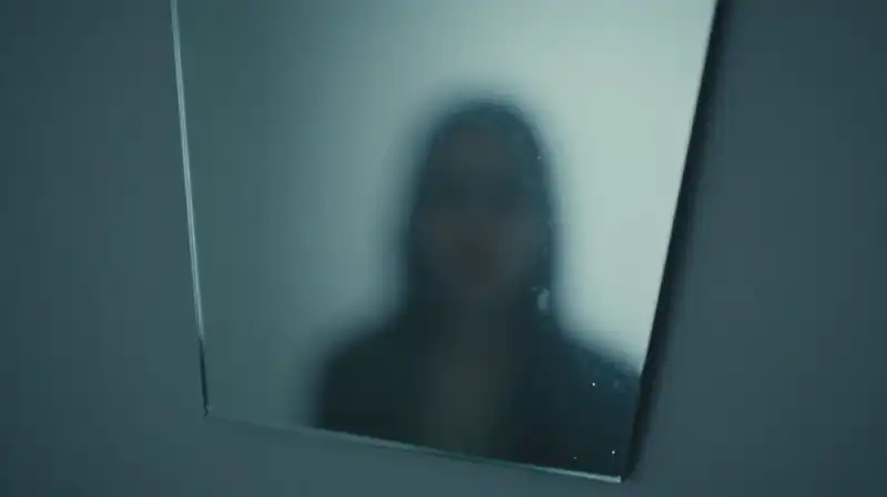 A blurred shape reflects in a fragmented, blue-toned mirror