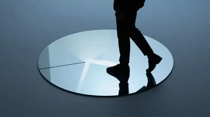 A silhouette steps into a circle of light amid reflections