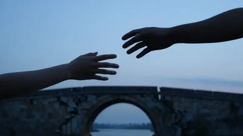 Two hands reach toward a fading silhouette on a crumbling bridge