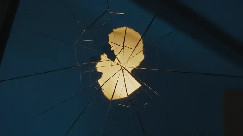 A golden silhouette reflects in a cracked, fragmented mirror