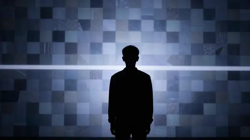 A silhouette stands before a shifting mosaic of geometric shapes