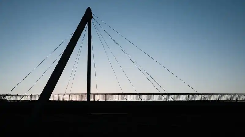 A silhouette walks across a glowing geometric bridge at dawn