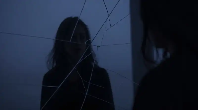 A lone silhouette reflects in a cracked, geometric mirror