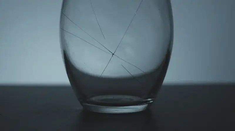 A fragile, cracked glass vessel emerges from a blue shadow