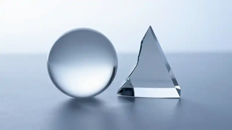 A glass sphere and fractured prism rest in blue shadows